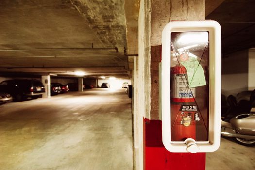 Fire extinguisher in an underground parking garage with parked cars.